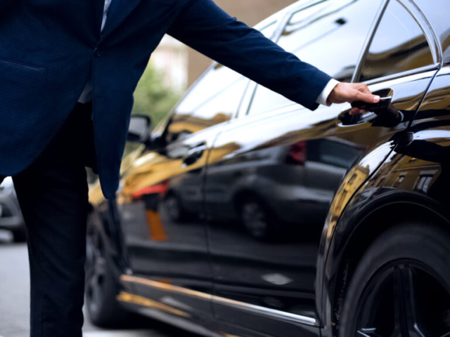 Personal driver opening backseat door in car for successful businessman, service